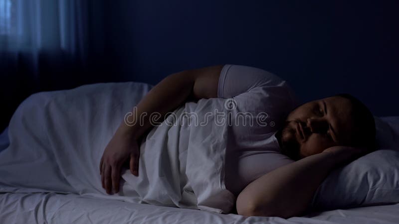 Homme obèse dormant dans le lit, détendant la nuit sur le matelas confortable, repos
