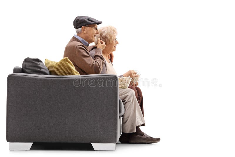 Homme plus âgé et femme s'asseyant sur un sofa et mangeant du maïs éclaté image libre de droits Homme plus âgé et femme s'asseyant sur un sofa et mangeant du maïs éclaté image libre de droits