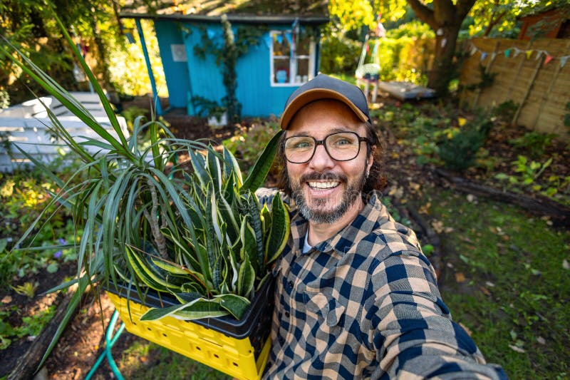 Homme prenant un selfie tenant une boîte de plantes en pot dans son jardin image libre de droits