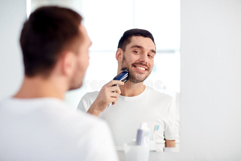 Homme rasant la barbe avec le trimmer à la salle de bains image stock Homme rasant la barbe avec le trimmer à la salle de bains image stock