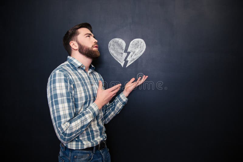 Homme romantique triste tenant le coeur brisé dessiné au-dessus du fond de tableau noir photo stock Homme romantique triste tenant le coeur brisé dessiné au-dessus du fond de tableau noir photo stock