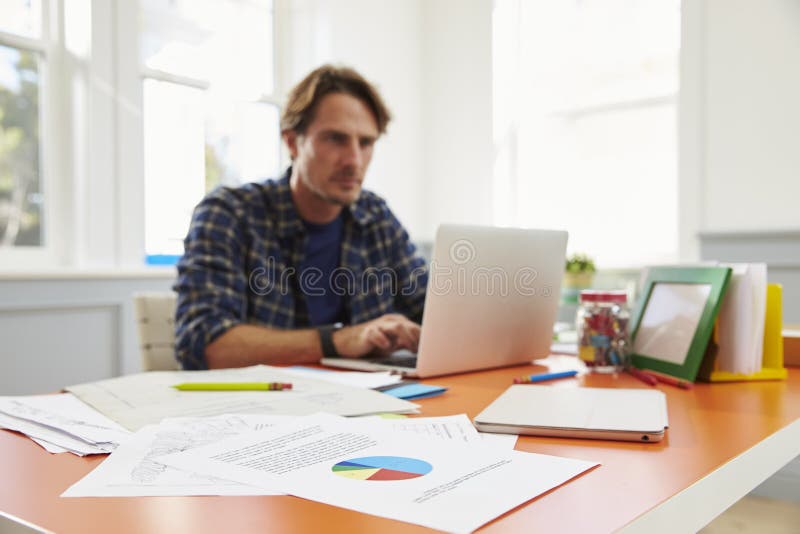 Homme s'asseyant au bureau fonctionnant à l'ordinateur portable dans le siège social photo stock Homme s'asseyant au bureau fonctionnant à l'ordinateur portable dans le siège social photo stock