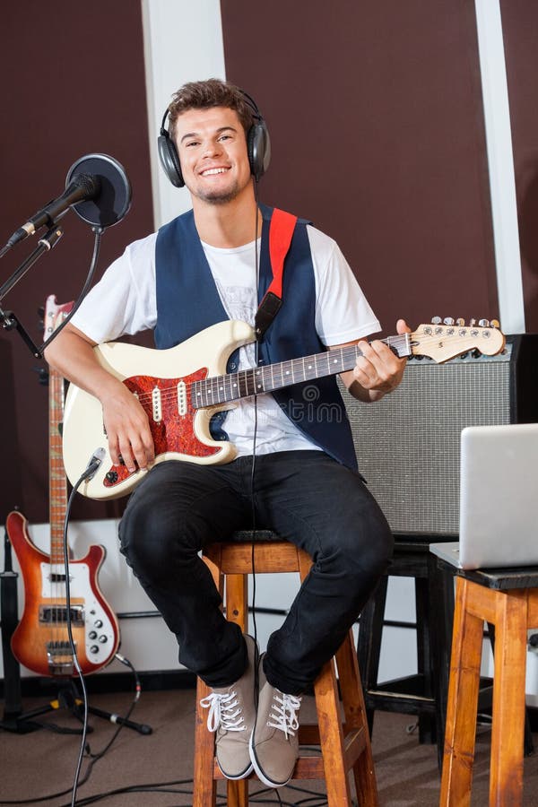 Homme sûr jouant la guitare tout en se reposant sur des selles image stock Homme sûr jouant la guitare tout en se reposant sur des selles image stock
