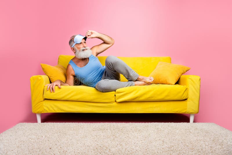 Homme senior se relaxant à l'intérieur sur canapé jaune contre mur rose embrassant le loisir et le confort photos stock