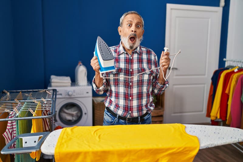 Homme supérieur sceptique grands yeux dans l'incrédulité donne un regard peu convaincu à la machine à fer dans la salle de blanchi image stock