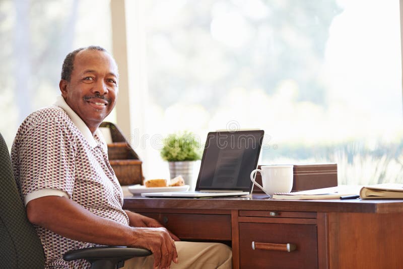 Homme supérieur à l'aide de l'ordinateur portable sur le bureau à la maison image libre de droits Homme supérieur à l'aide de l'ordinateur portable sur le bureau à la maison image libre de droits