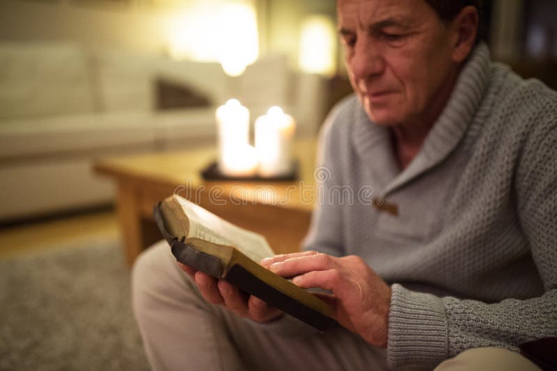 Homme supérieur à la maison lisant la bible, bougies brûlantes derrière lui photos libres de droits
