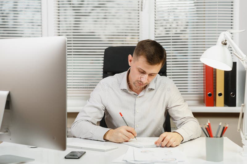 Homme sérieux et rédigé d'affaires dans la chemise se reposant au bureau, fonctionnant à l'ordinateur avec le moniteur moderne Di photographie stock libre de droits Homme sérieux et rédigé d'affaires dans la chemise se reposant au bureau, fonctionnant à l'ordinateur avec le moniteur moderne Di photographie stock libre de droits