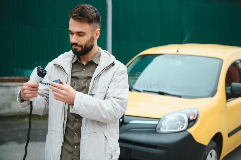 Homme tenant câble de charge électrique voiture électrique dans le parking extérieur. et il va connecter la voiture à la charge. et il va connecter la voiture à la station de charge dans le parking près du centre commercial.