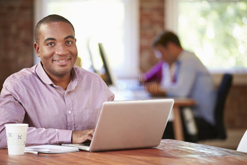 Homme travaillant à l'ordinateur portable dans le bureau contemporain photographie stock Homme travaillant à l'ordinateur portable dans le bureau contemporain photographie stock