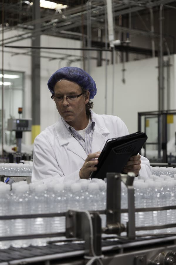 Homme à l'usine de mise en bouteilles inspectant l'eau en bouteille sur le convoyeur photographie stock libre de droits Homme à l'usine de mise en bouteilles inspectant l'eau en bouteille sur le convoyeur photographie stock libre de droits