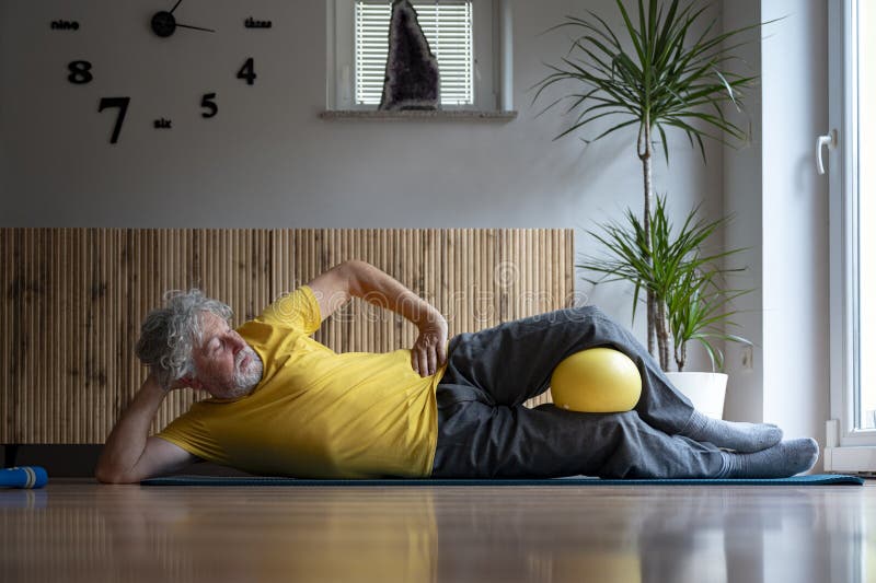 Homme âgé en tshirt jaune vif pratique pilates exercice avec une balle photo libre de droits