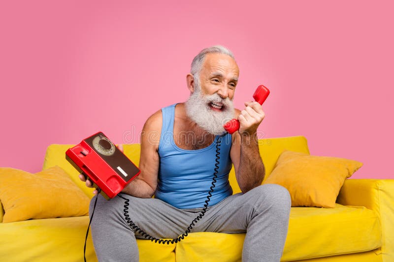 Homme âgé jouissant d'un moment avec le téléphone rotatif sur canapé jaune sur fond rose image libre de droits