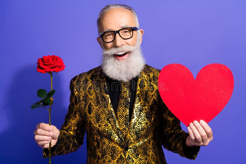 Homme élégant joyeux tenant un coeur rouge et rose sur fond violet portant un costume doré photographie stock