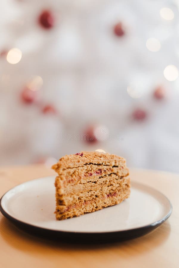 Honey cake on the table near the white Christmas tree with golden bokeh lights