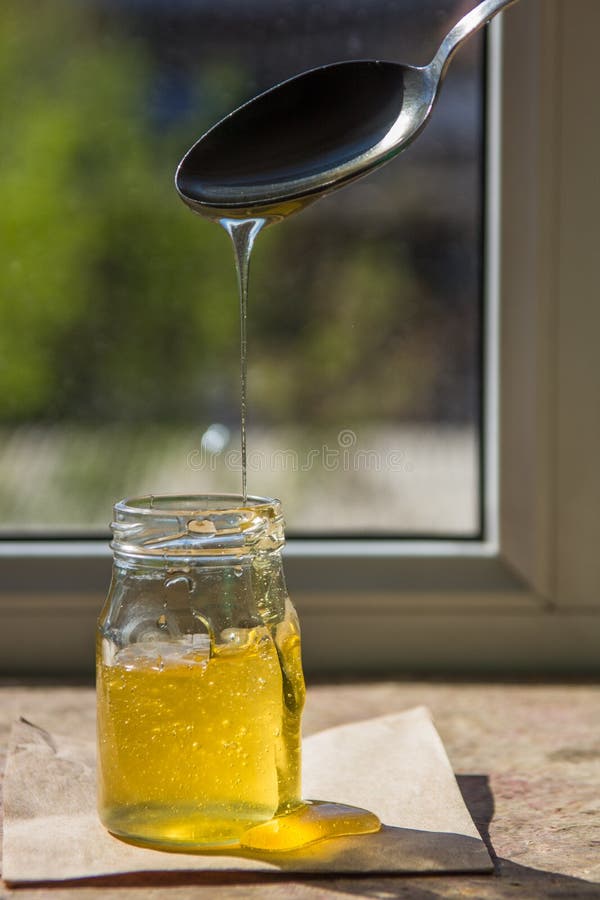 Honey Dripping from a Spoon. Organic Pure Honey in Jar Stock Image