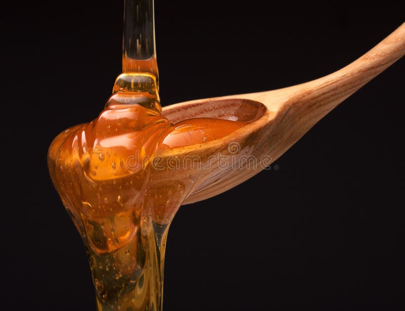 Honey dripping from a wooden honey dipper on black background