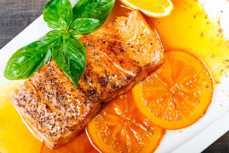 Honey Glazed fillet salmon with orange slices, spices and basil on white plate on dark background.