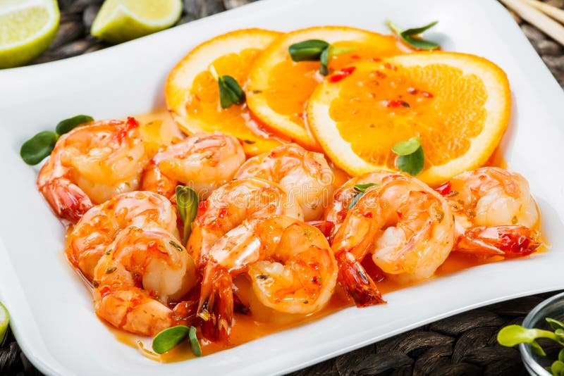 Honey Glazed Shrimp with orange slices, spices and sunflower sprouts on white plate on bamboo background