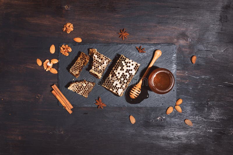 Honeycomb, bee pollen granules, honey jar with wooden dipper, almond nuts on black slate tray over dark background. Copy space.