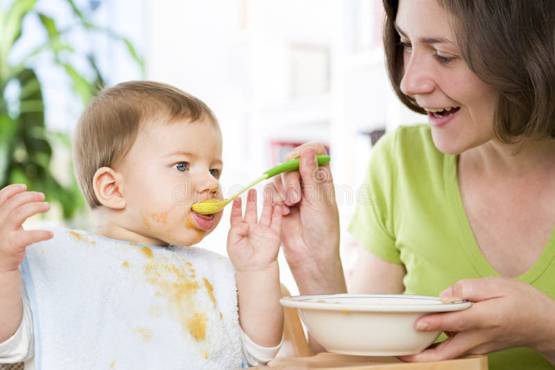 Hongerige babyjongen die voedsel naast zijn moeder eten. stock fotografie Hongerige babyjongen die voedsel naast zijn moeder eten. stock fotografie
