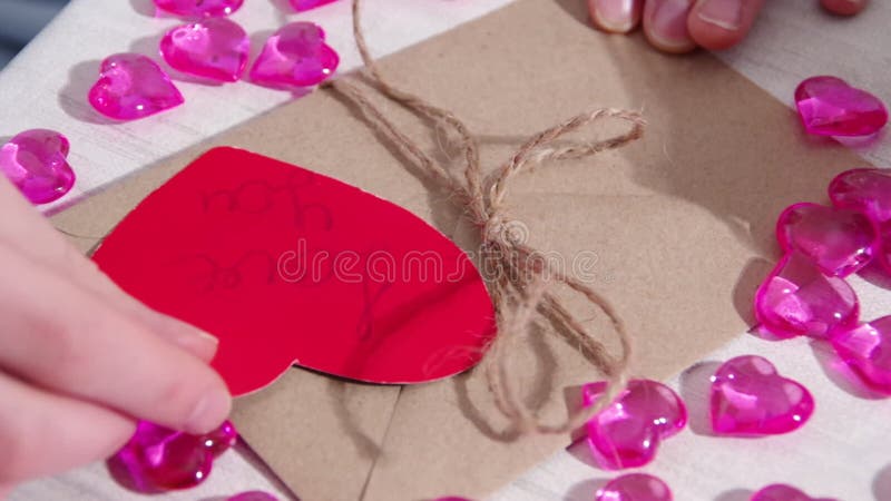 Honhänder som dekorerar ett pappersformat och ett rött pappershjärta med inskriften är älskar dig. omslagning av valentinpresenter