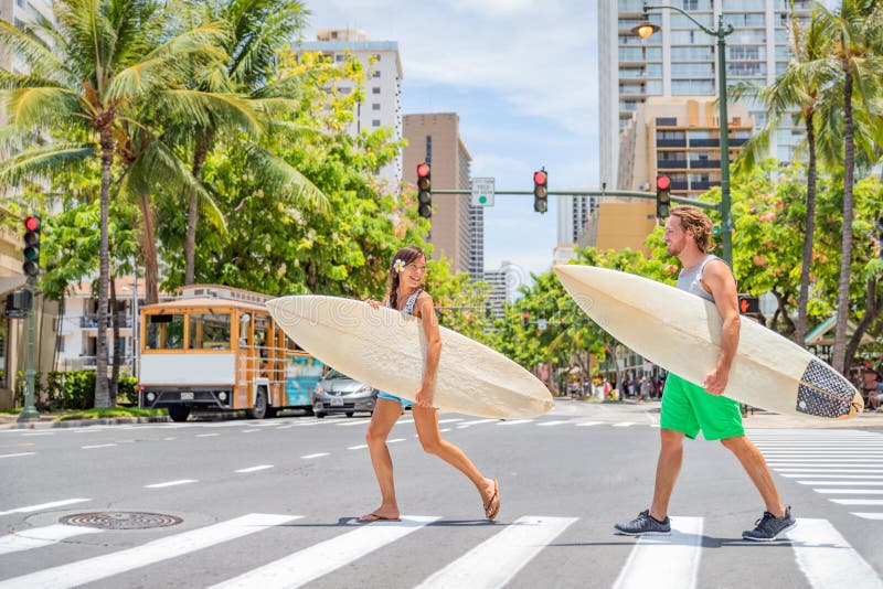 Honolulu Hawaii surfers couple tourists people walking crossing city street carrying surfboards going to the beach