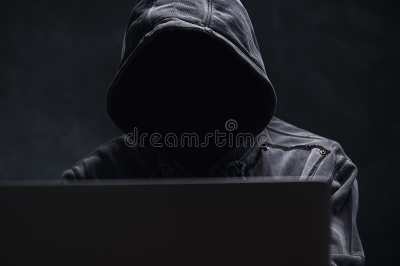 Hooded computer hacker using laptop computer royalty free stock photography