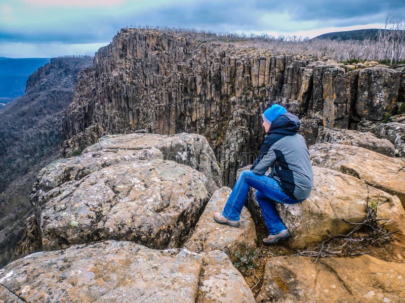 Senior perched on rocks at Devil`s Gullet, Tasmania, Australia looking out into a steep, narrow glacial gorge formed by vertical dolerite cliffs, 220m high . Senior perched on rocks at Devil`s Gullet, Tasmania, Australia looking out into a steep, narrow glacial gorge formed by vertical dolerite cliffs, 220m high