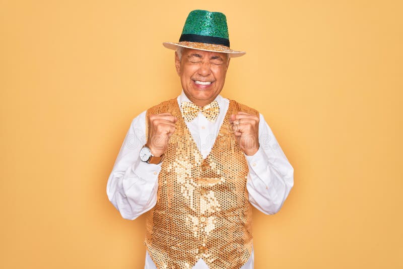 Middle age senior grey-haired man wearing Brazilian carnival custome over yellow background excited for success with arms raised and eyes closed celebrating victory smiling. Winner concept. Middle age senior grey-haired man wearing Brazilian carnival custome over yellow background excited for success with arms raised and eyes closed celebrating victory smiling. Winner concept