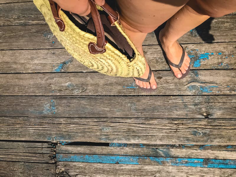 Hoogste mening, foto van benen in strandwipschakelaars en met een strozak ter beschikking op een houten oude vloer Foto's op vaka royalty-vrije stock afbeelding Hoogste mening, foto van benen in strandwipschakelaars en met een strozak ter beschikking op een houten oude vloer Foto's op vaka royalty-vrije stock afbeelding