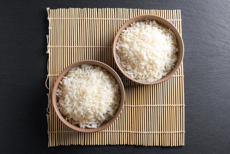 Hoogste mening: gestoomde gekookte basmati rijst in ronde ceramische kommen over zwarte steen