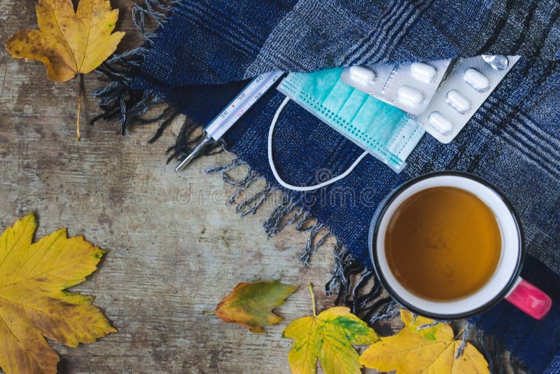Hoogste mening van een kop thee, een blauwe sjaal, een thermometer, drugs en medische gezichtsmasker en bladeren op houten achter royalty-vrije stock foto Hoogste mening van een kop thee, een blauwe sjaal, een thermometer, drugs en medische gezichtsmasker en bladeren op houten achter royalty-vrije stock foto