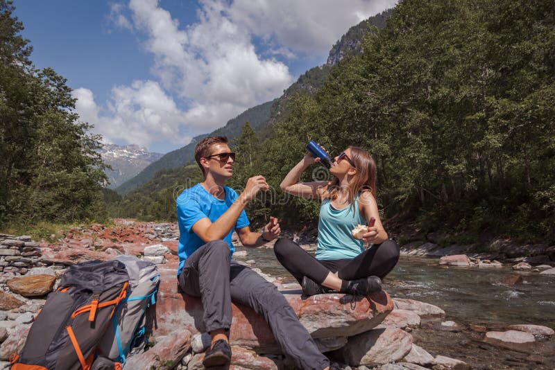 Hora de la almuerzo de los pares de los Backpackers con el landjaeger y pan en un r?o fotografía de archivo libre de regalías Hora de la almuerzo de los pares de los Backpackers con el landjaeger y pan en un r?o fotografía de archivo libre de regalías