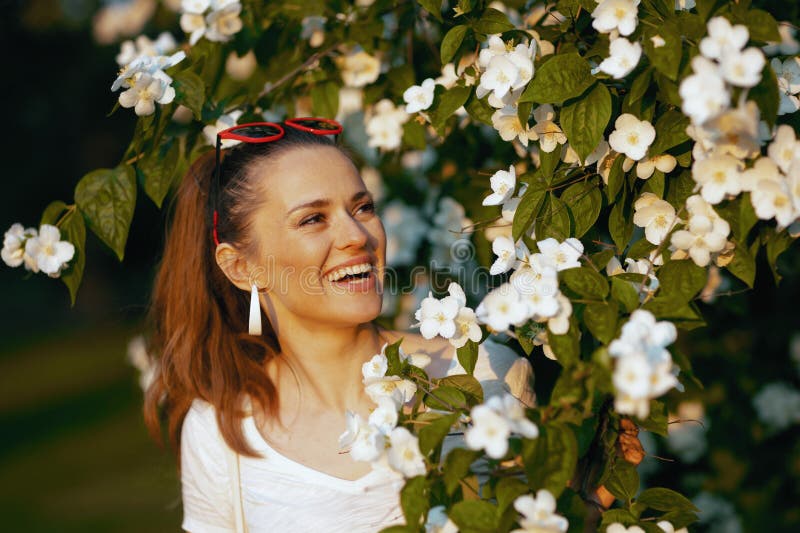 Summer time. smiling middle aged woman in white shirt near flowering tree. Summer time. smiling middle aged woman in white shirt near flowering tree