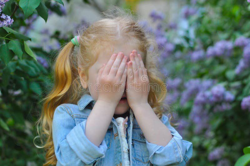 Little girl playing hide and seek in a flowering garden. Little girl playing hide and seek in a flowering garden