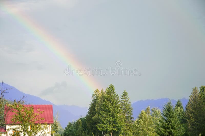 Horizontal de montagne Arc-en-ciel et rayons de soleil au-dessus de village photo stock Horizontal de montagne Arc-en-ciel et rayons de soleil au-dessus de village photo stock