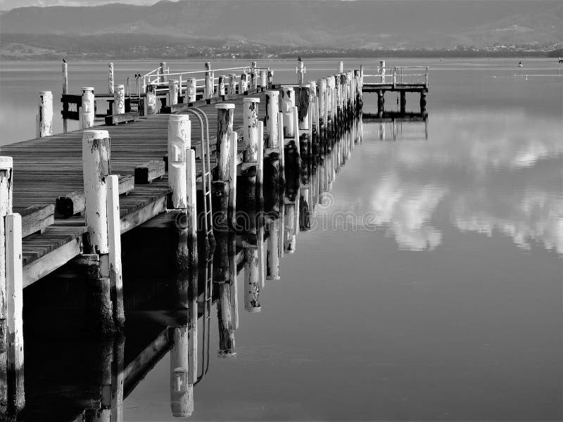 Horizontal greyscale shot of a wooden pier on the peaceful Illawarra lake