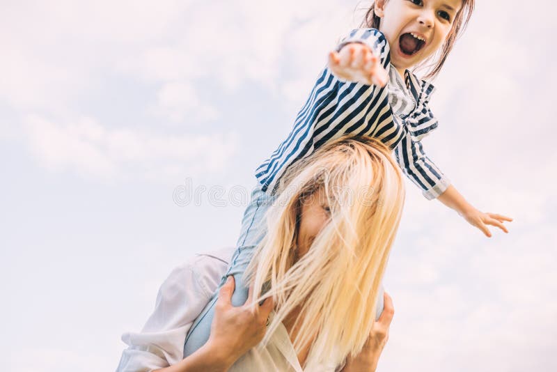 Horizontal image of happy little daughter on a piggy back ride with her smiling mother on sky background. Loving woman and her royalty free stock photography Horizontal image of happy little daughter on a piggy back ride with her smiling mother on sky background. Loving woman and her royalty free stock photography