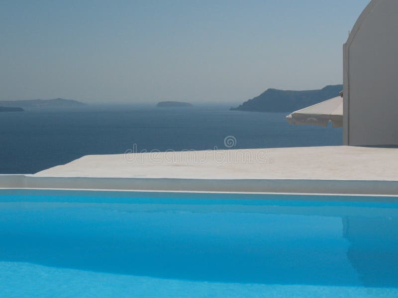 Horizontal image of a serene blue infinity pool overlooking the deep blue Aegean Sea, with islands visible on the horizon. stock photo