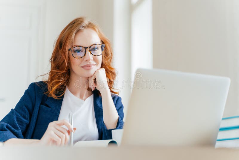 Horizontal shot of pleasant looking successful professional female lawyer learns clients case, works on modern laptop computer