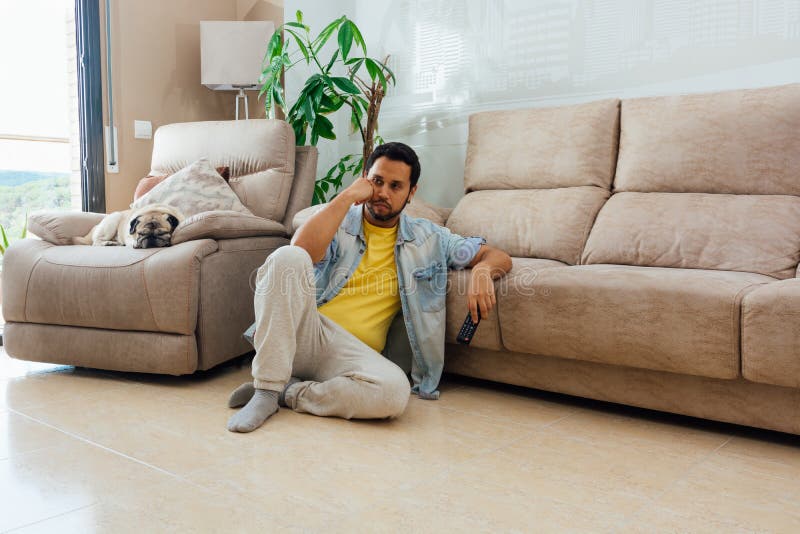 A horizontal shot of a male sitting on the floor and watching a TV with remote control in his hand. A horizontal shot of a male sitting on the floor and watching a TV with remote control in his hand