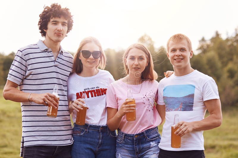 Horizontaler Schuss von freundlichen glücklichen vier Jugendlichen stehen nah an einander, tragen zufällige T-Shirts, Griffflasch stockfotos Horizontaler Schuss von freundlichen glücklichen vier Jugendlichen stehen nah an einander, tragen zufällige T-Shirts, Griffflasch stockfotos