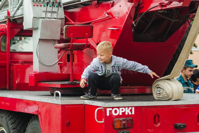 HORKI, BIELORUSSIA - 25 LUGLIO 2018: Il ragazzo gioca sulle automobili rosse del servizio di salvataggio 112 di una festa nel par immagine stock libera da diritti HORKI, BIELORUSSIA - 25 LUGLIO 2018: Il ragazzo gioca sulle automobili rosse del servizio di salvataggio 112 di una festa nel par immagine stock libera da diritti