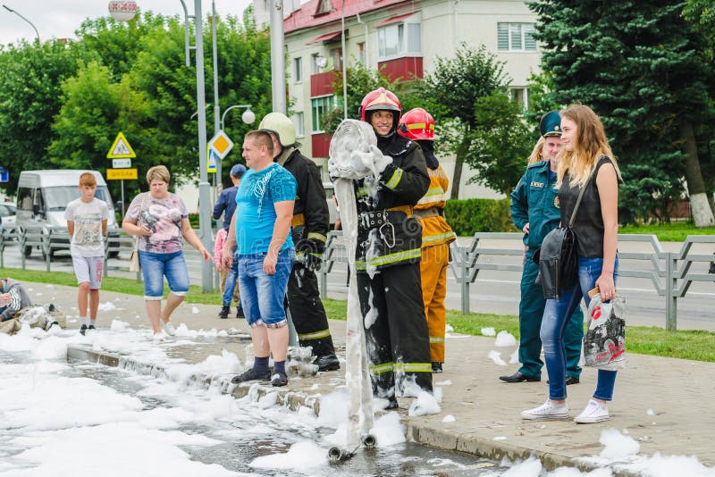 HORKI, BIELORUSSIA - 25 LUGLIO 2018: Volte dell'ufficiale 112 di salvezza la manichetta antincendio ed i colloqui con un sorriso fotografia stock libera da diritti HORKI, BIELORUSSIA - 25 LUGLIO 2018: Volte dell'ufficiale 112 di salvezza la manichetta antincendio ed i colloqui con un sorriso fotografia stock libera da diritti