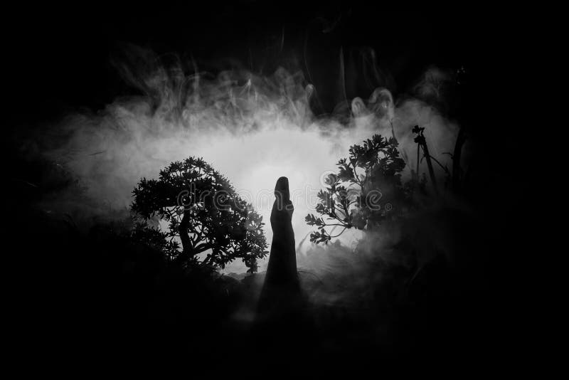 Horror Halloween decorated conceptual image. Alone girl with the light in the forest at night. Silhouette of girl standing between