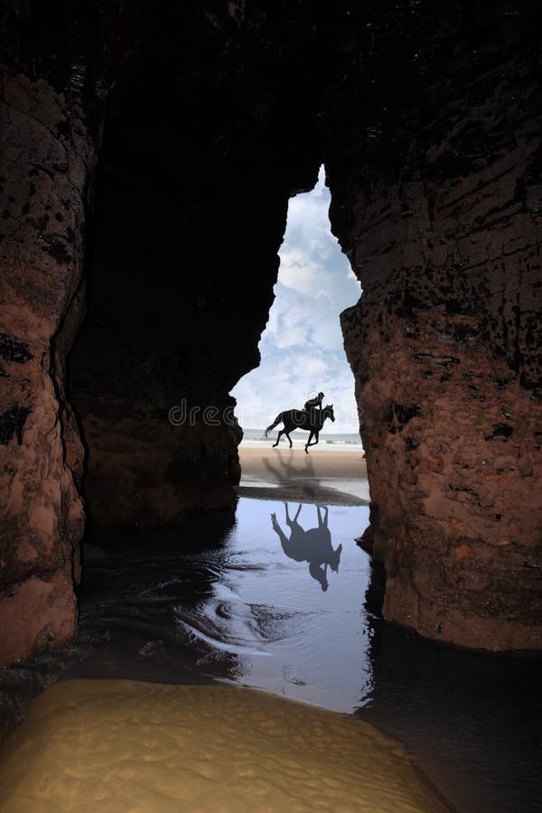 Cliff jeskyně v ballybunion county kerry v irsku se siluetou koně a jezdce cvalu na pláži.