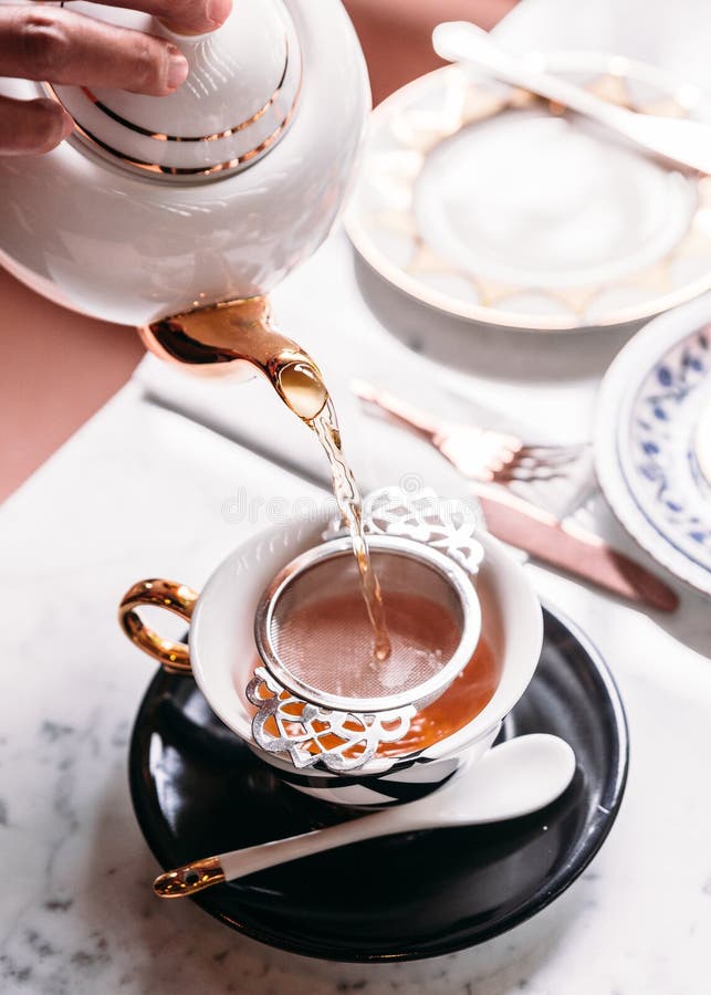 Hot Apple Tea served by pouring from mug through stainless steel tea strainer infuser in porcelain vintage cup