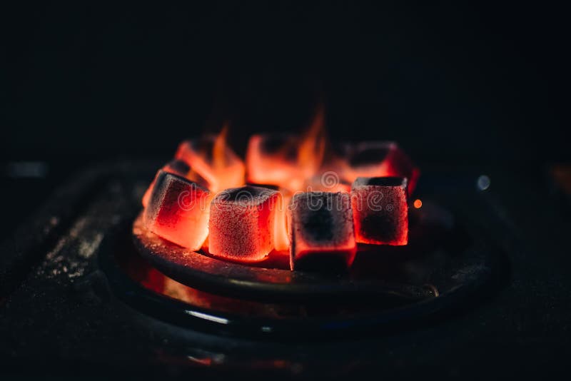 Hot red coals for Shisha warmed up on the stove in a hookah bar on a dark background. Hot red coals for Shisha warmed up on the stove in a hookah bar on a dark background