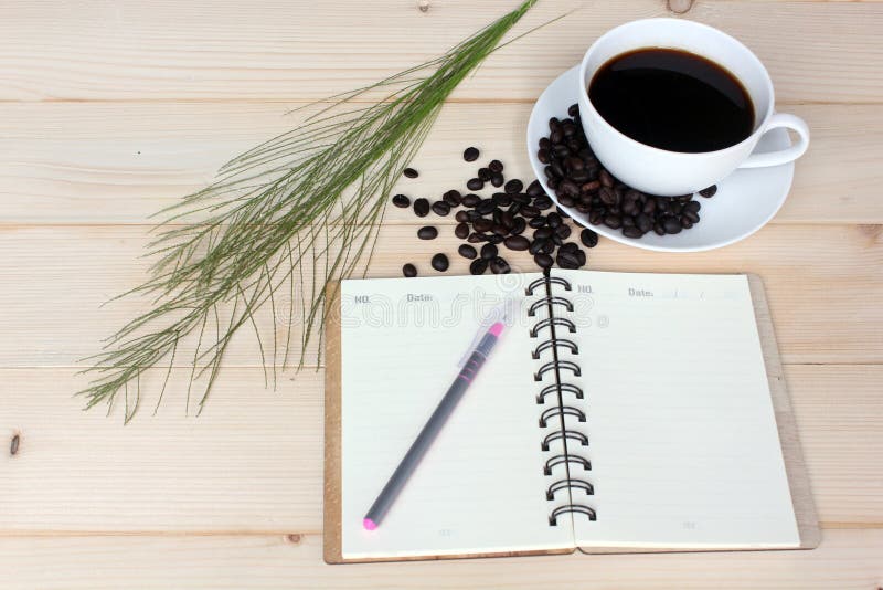 Hot Coffee and beans with Notebook on wooden board. Hot Coffee and beans with Notebook and pen on wooden board royalty free stock photo Hot Coffee and beans with Notebook on wooden board. Hot Coffee and beans with Notebook and pen on wooden board royalty free stock photo